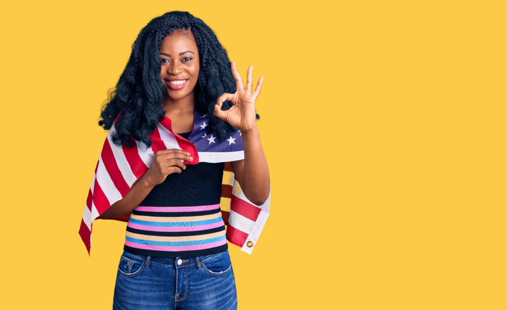 beautiful african american woman holding united states flag doing ok sign with fingers, smiling friendly gesturing excellent symbol
