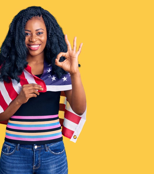beautiful african american woman holding united states flag doing ok sign with fingers, smiling friendly gesturing excellent symbol